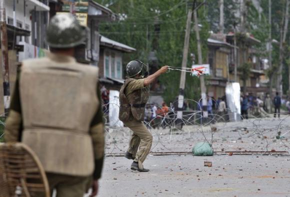 An Indian policeman throws a stone towards Kashmiri protesters during an anti-election protest in Baramulla district